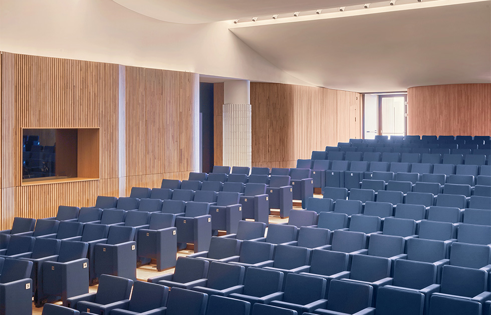 View of the auditorium, featuring tiered seating and warm wooden accents designed for optimal acoustics and comfort.